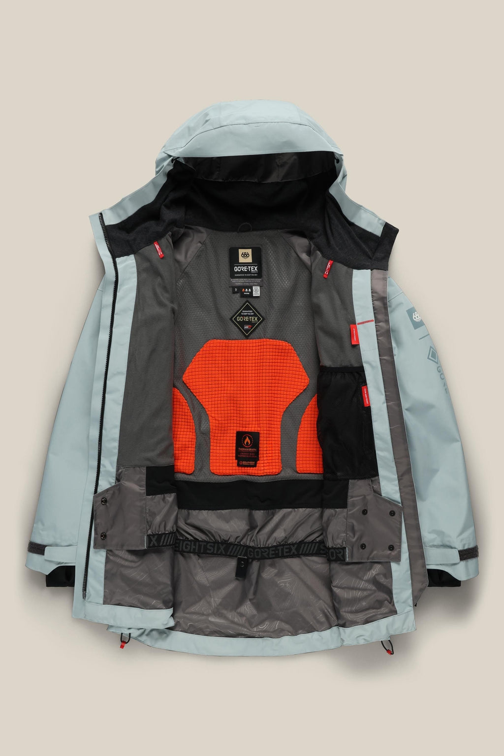 The 686 Women's GORE-TEX Skyline Thermagraph® Jacket by 686 is shown flat and unzipped, displaying its orange mesh lining, interior labels and pockets, and black and red accents on the light blue and gray waterproof shell.