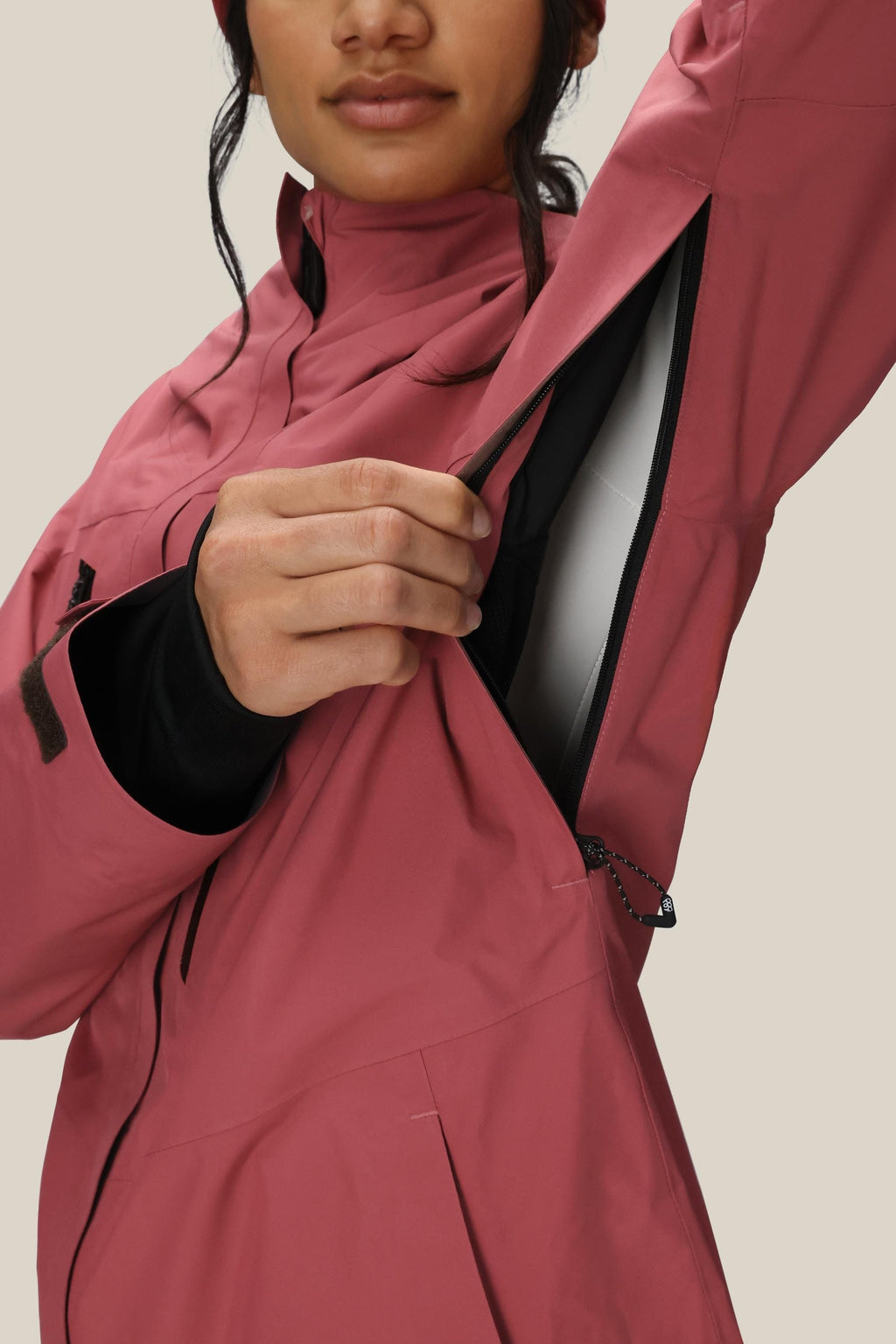 A woman in the 686 Women's GORE-TEX Skyline Thermagraph® Jacket unzips an underarm vent to reveal the lining. Her face is partially visible as she stands against a plain background.
