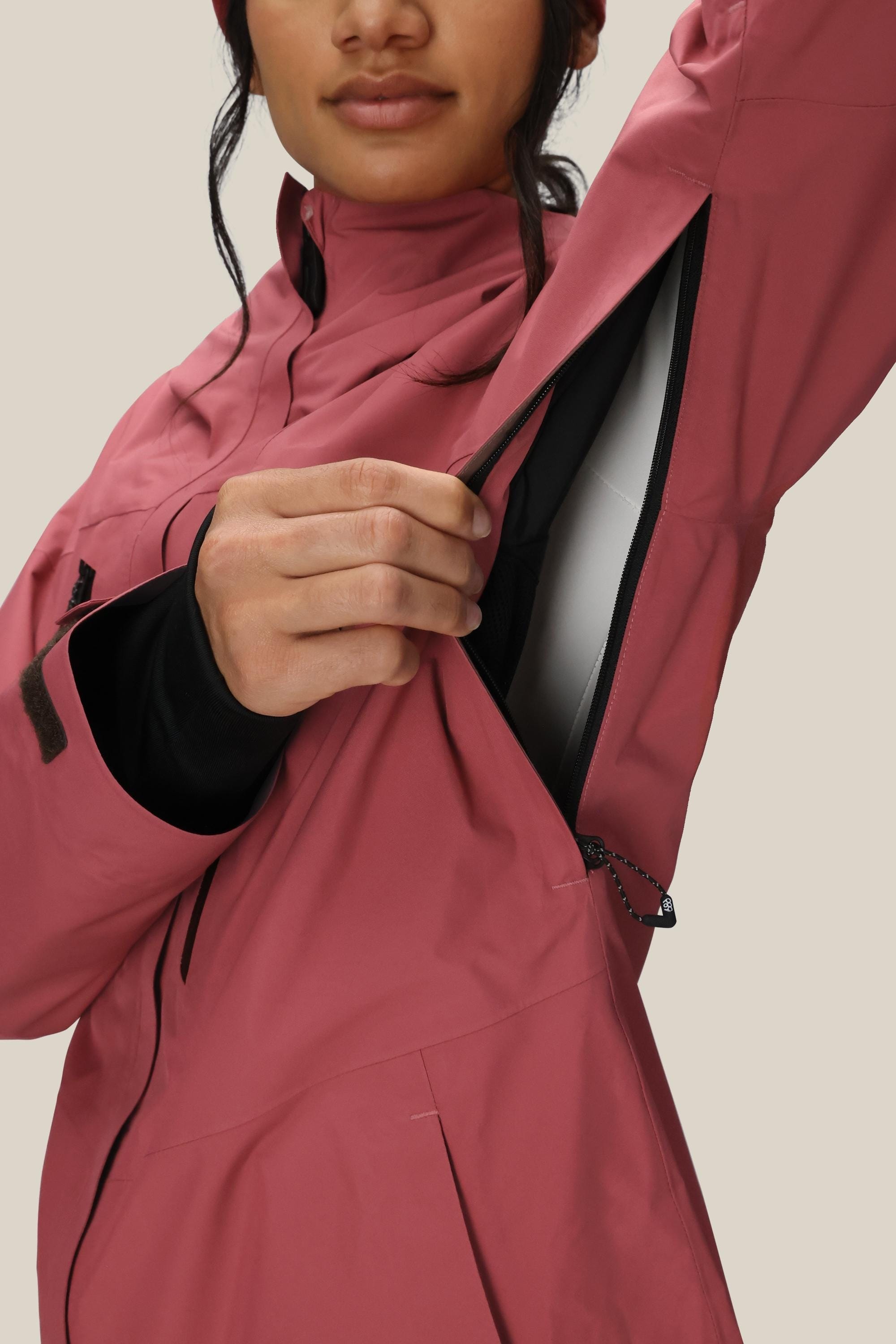 A woman in the 686 Women's GORE-TEX Skyline Thermagraph® Jacket unzips an underarm vent to reveal the lining. Her face is partially visible as she stands against a plain background.