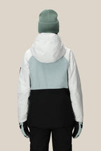 A person is shown from the back, wearing the 686 Women's GORE-TEX Willow™ Insulated Jacket by 686 in a white, light grey, and black color-block design with a light green beanie, against a plain beige background—perfect for winter outings.