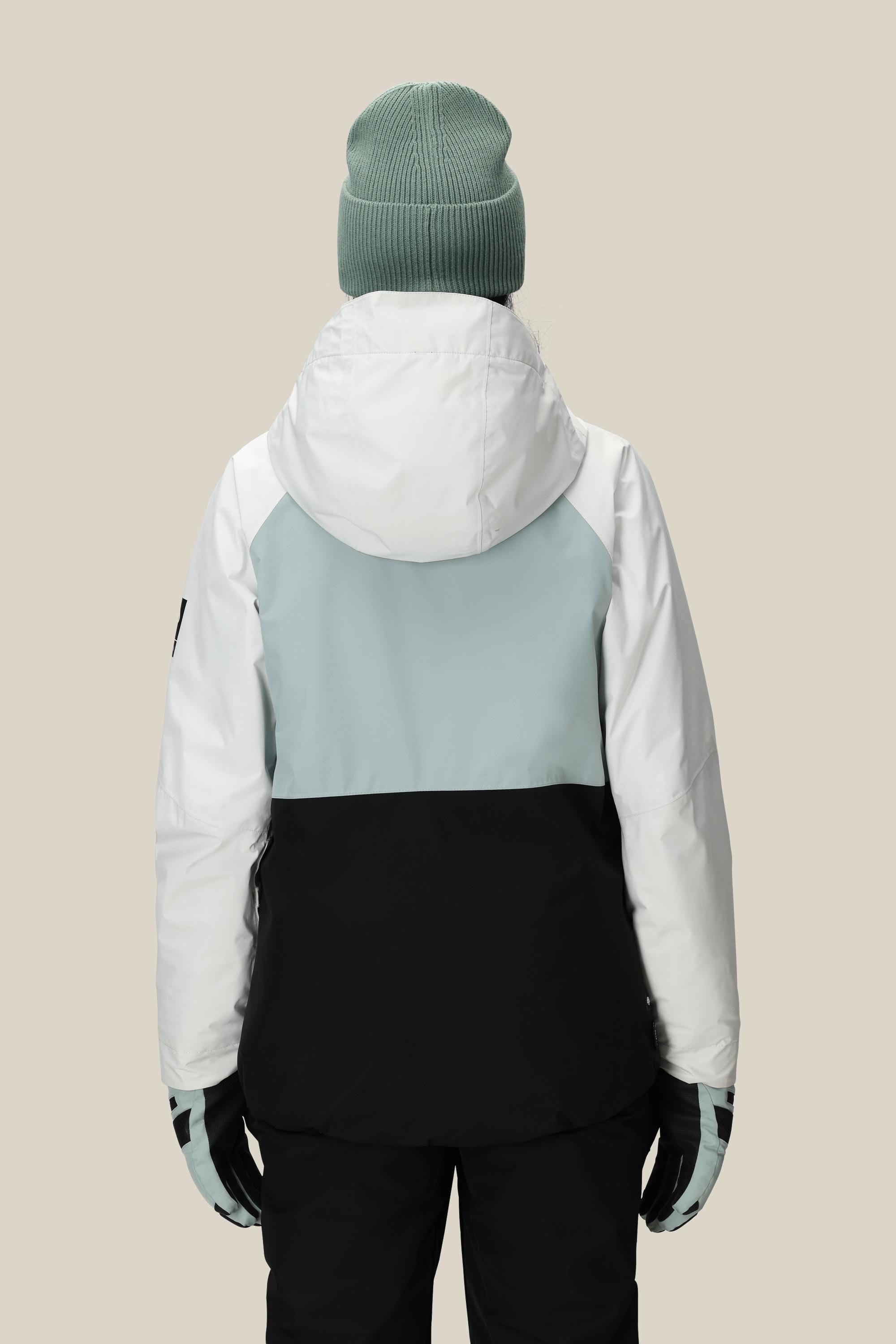 A person is shown from the back, wearing the 686 Women's GORE-TEX Willow™ Insulated Jacket by 686 in a white, light grey, and black color-block design with a light green beanie, against a plain beige background—perfect for winter outings.