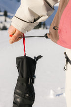 A person in the 686 Women's GORE-TEX Willow™ Insulated Jacket tightens the drawstring of a black pouch at their waist, with snowy ground and trees blurred in the background.