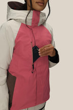 A woman wearing the 686 Women's GORE-TEX Willow™ Insulated Jacket in pink and white puts a black smartphone into its zippered chest pocket. The background is plain and light-colored.