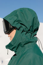 Wearing the 686 Women's Whisper™ Insulated Jacket and black ski goggles, a woman stands outdoors in bright sunlight with a snowy landscape and clear blue sky in the background.