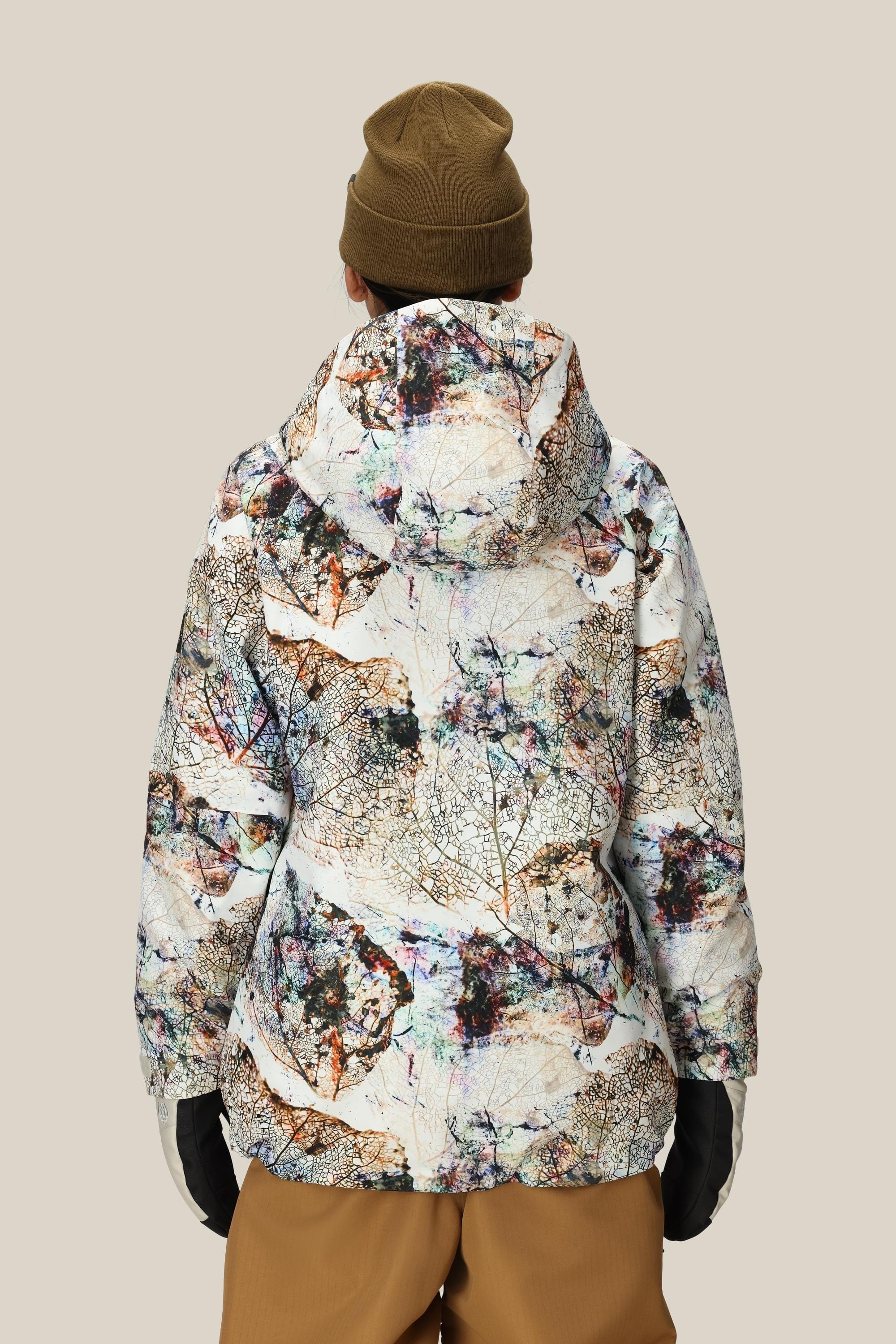 A woman stands with her back to the camera, wearing a 686 Women's Whisper™ Insulated Jacket with a hood, brown pants, black gloves, and a brown beanie against a plain beige background.