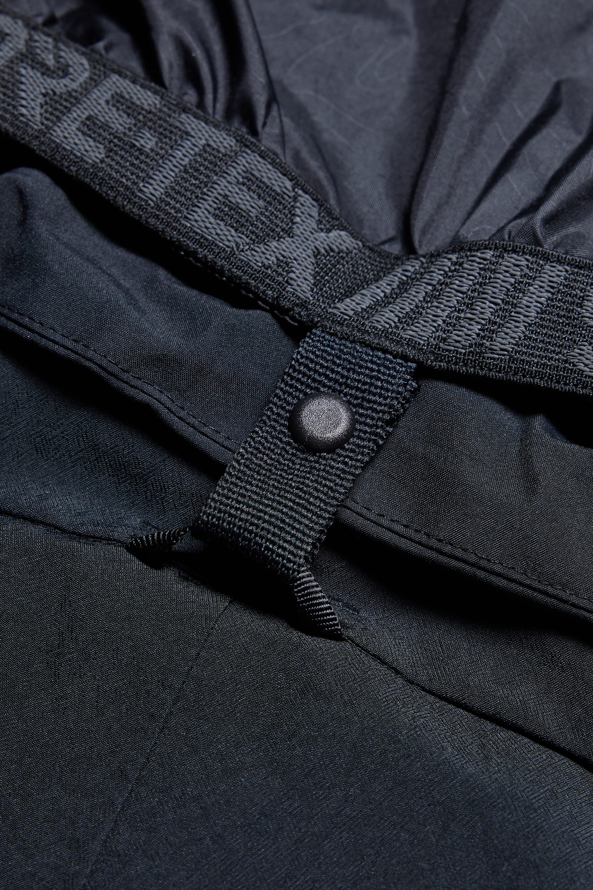 Close-up of the 686 Women's Whisper™ Insulated Jacket shows a textured button, fabric loop, elastic waistband, and partially visible GORE-TEX text. The durable polyester from 686 appears water-resistant.