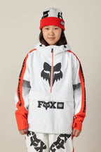 A person wearing the 686 Women's Fox Racing Shell Anorak, featuring a bold black fox logo, poses against a plain beige background.