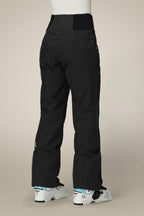 A person is shown from the back wearing 686 Women's GORE-TEX Willow™ Insulated Pant in black with white ski boots, standing against a plain beige background.
