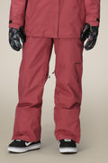 A person wears 686 Women's GORE-TEX Willow™ Insulated Pants in rose, paired with a matching jacket, patterned gloves, and black-and-white sneakers against a neutral background.