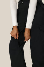 A woman in a white long-sleeve top uses both hands to open a zippered thigh vent on the 686 Women's Aura™ Insulated Cargo Pant.