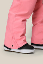 A close-up of a person standing on a light beige surface, wearing the 686 Women's Aura™ Insulated Cargo Pant in pink and black winter boots with white soles.