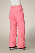 A person stands with their back to a beige background, wearing the 686 Women's Aura™ Insulated Cargo Pant in bright pink and black sneakers with white soles.