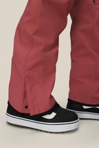 Close-up of a person wearing the 686 Women's Aura™ Insulated Cargo Pant in a loose fit, rose color, paired with black-and-white sneakers. The pants feature snap button detail near the ankle and slightly cover the shoes, set against a plain light background.