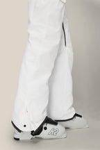 A person stands on a light surface wearing 686 Women’s Aura™ Insulated Cargo Pants in white and white ski boots featuring a black “K2” logo. The image highlights the lower legs and feet.