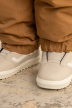 Someone wearing 686 Women's Outline™ Shell Pant by 686, paired with light beige slip-on sneakers, stands on a textured, slightly worn surface.