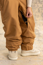 A person wearing 686 Women's Outline™ Shell Pant in brown and white sneakers stands on a light mottled surface, with only the lower half of their body visible.