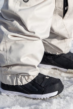 Close-up of a person wearing 686 Women's Outline™ Shell Pant in off-white with black winter shoes, standing on snow.