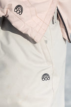 Close-up of a person wearing 686 Women's Outline™ Shell Pant in light beige and a pale pink jacket, both with matching black embroidered rainbow patches and three small circles. Brand: 686.