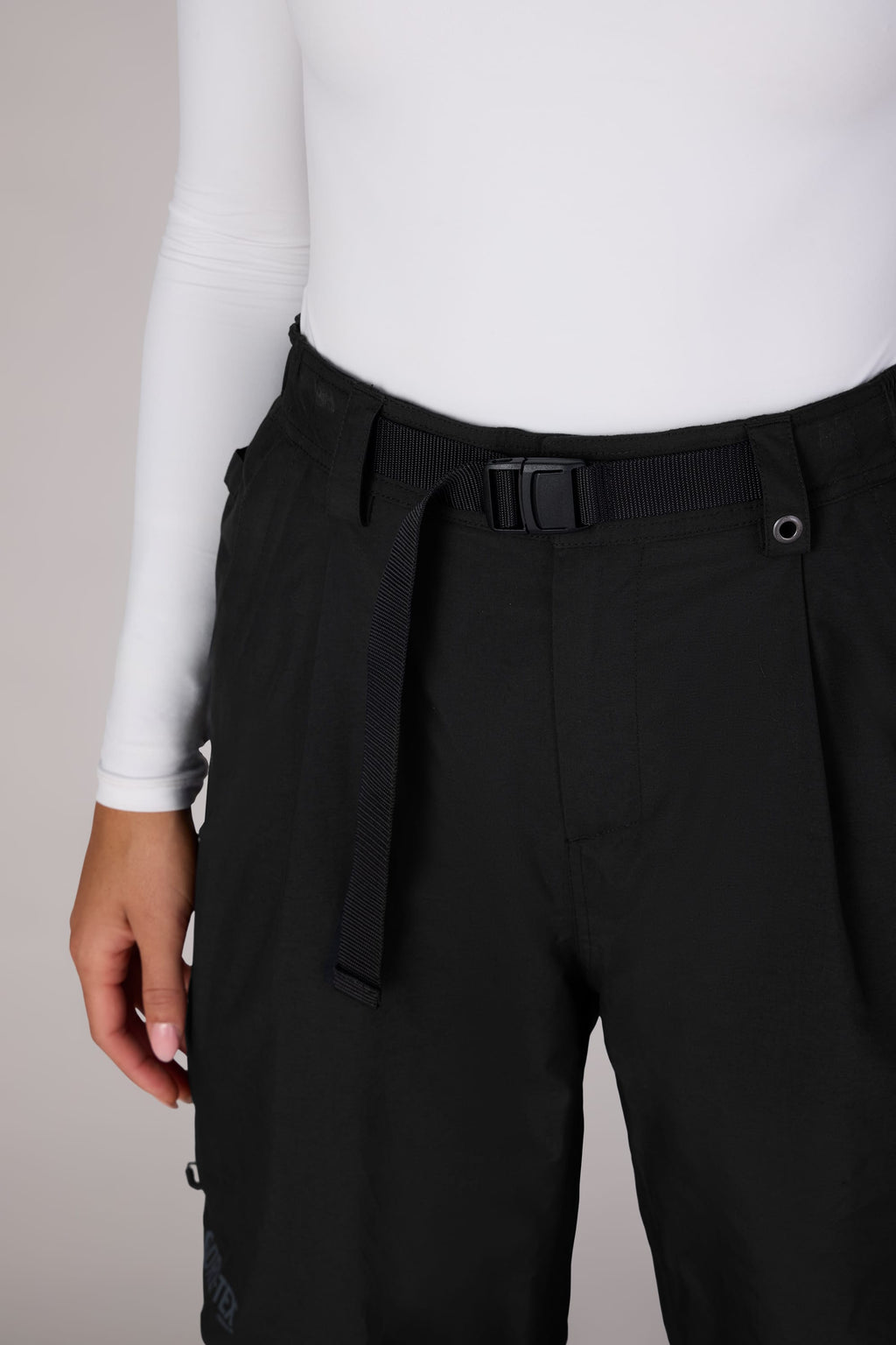 A person wearing a white long-sleeve top and 686 Women's GORE-TEX Outline™ Shell Pant, shown from torso to mid-thigh against a plain background.