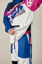 A person in the 686 Men's Fox Racing Waterproof Hoody shows the large side zipper being unzipped to reveal an inner pocket. The hoody features blue, white, pink, and black patterns; only the torso and part of the legs are visible.