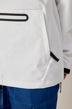 A close-up of a person wearing the 686 Women's Hello Kitty® Waterproof Hoody, featuring a faint Hello Kitty face design on the front pocket, paired with blue checkered pants. The person's hand is partially visible on the right.