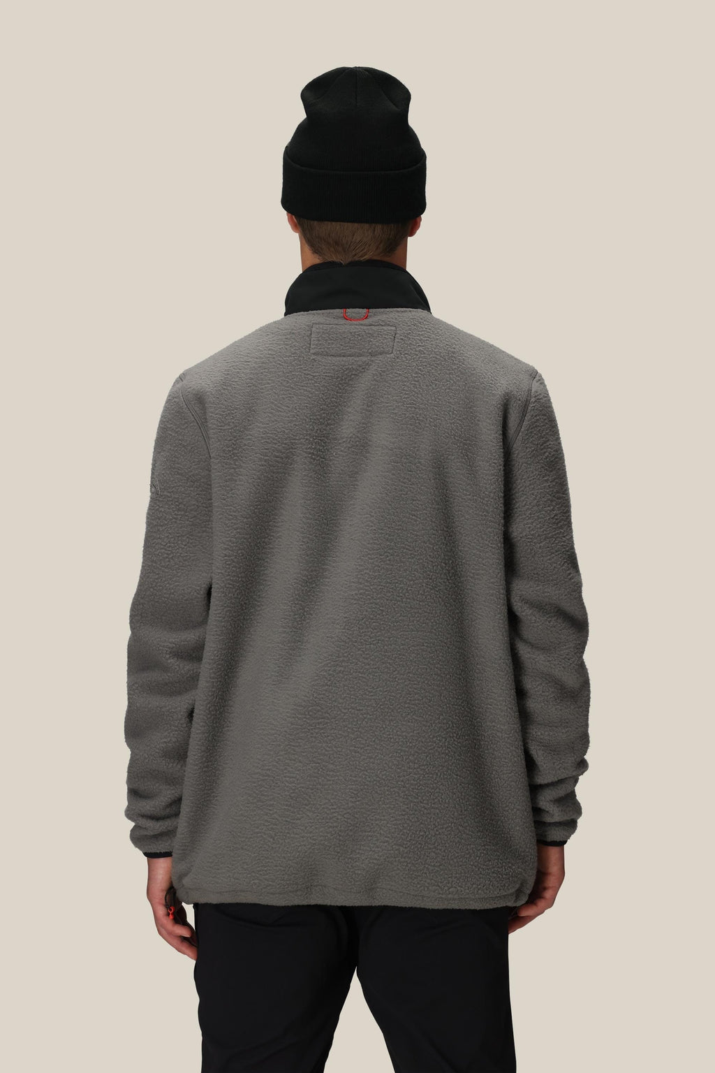 A person wearing a black beanie and the 686 Mens Tioga Fleece Pullover by 686 stands with their back to the camera against a plain beige background.