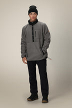 A man faces forward against a neutral background, wearing a black beanie, black pants, brown hiking boots, and the 686 Mens Tioga Fleece Pullover by 686—a grey polyester sweatshirt pullover with buttons.