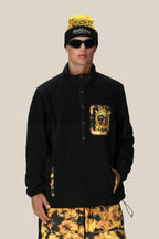 A person wearing the 686 Mens Sublime Tioga Fleece Pullover, featuring a colorful sun graphic, paired with yellow and black tie-dye shorts, a matching beanie, and sunglasses, stands with one hand in their pocket against a neutral background.