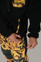 A person zips the pocket of yellow and black tie-dye pants while wearing a 686 Mens Sublime Tioga Fleece Pullover, with only their torso and hands visible.