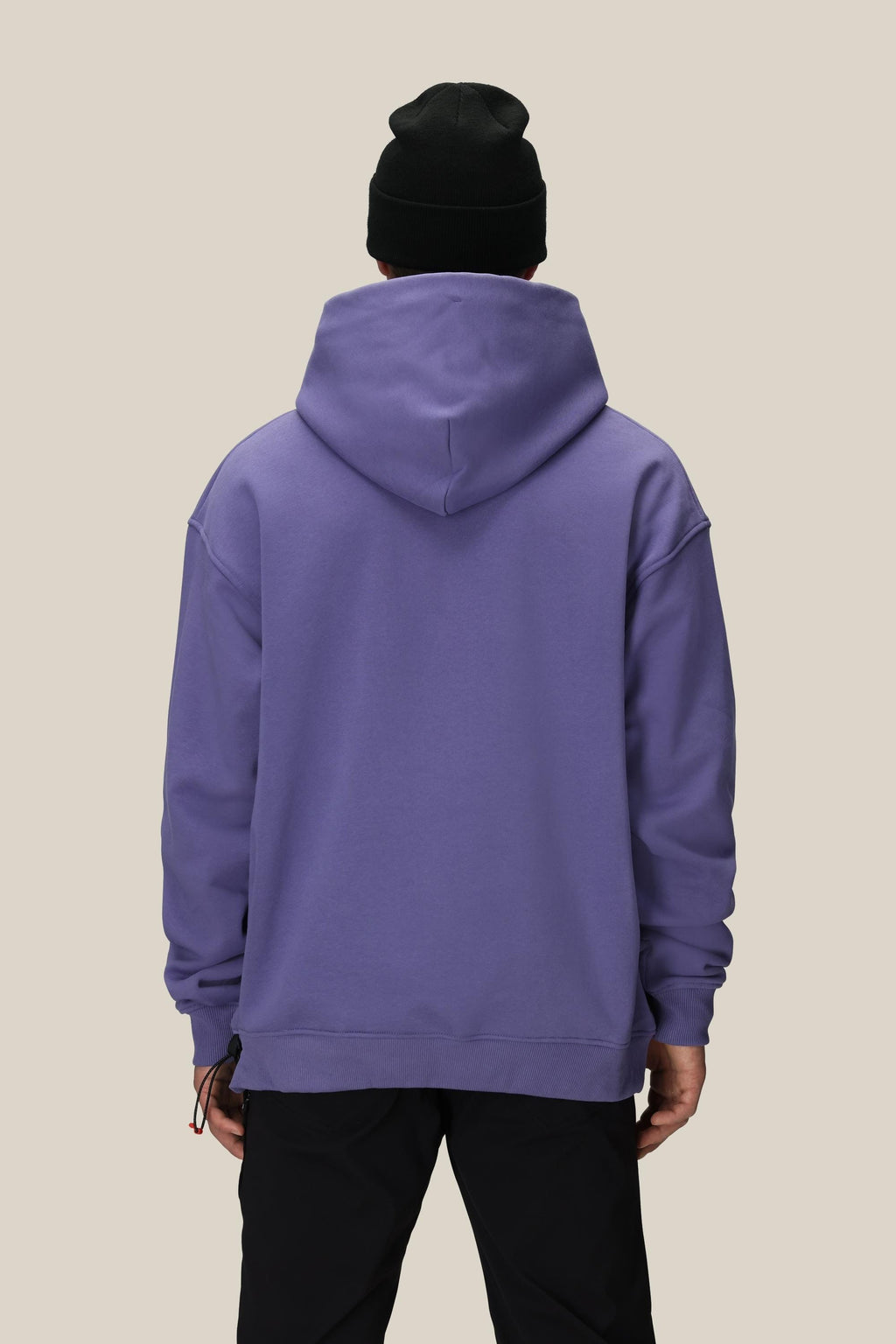 A person faces away from the camera against a plain beige background, wearing a black beanie, black pants, and the 686 Knockout Logo Premium Heavyweight Pullover Hoody by 686 in purple.