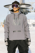 A man stands on snow with a ski lift in the background, wearing a gray hooded ski jacket, black pants, goggles, and 686 Men's GORE-TEX SMARTY® 3-In-1 Gauntlet Mitts by 686.
