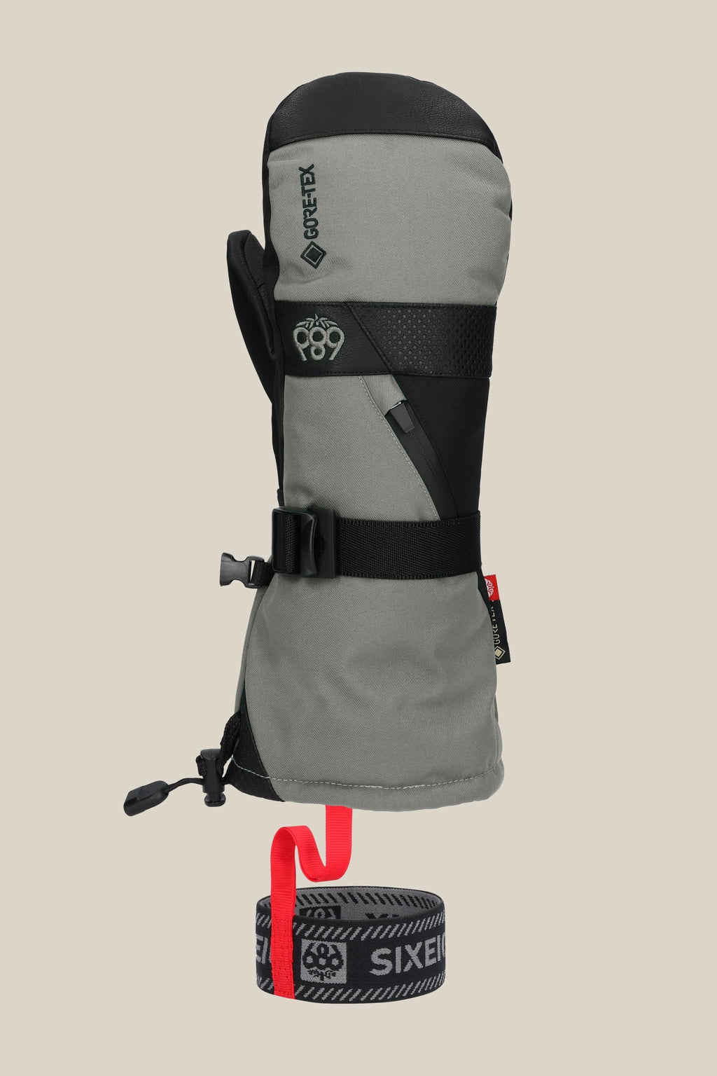 The 686 Men's GORE-TEX SMARTY® 3-In-1 Gauntlet Mitt is a gray and black mitt with a black strap, buckles, red pull tab, and Gore-Tex branding, shown on a beige background.