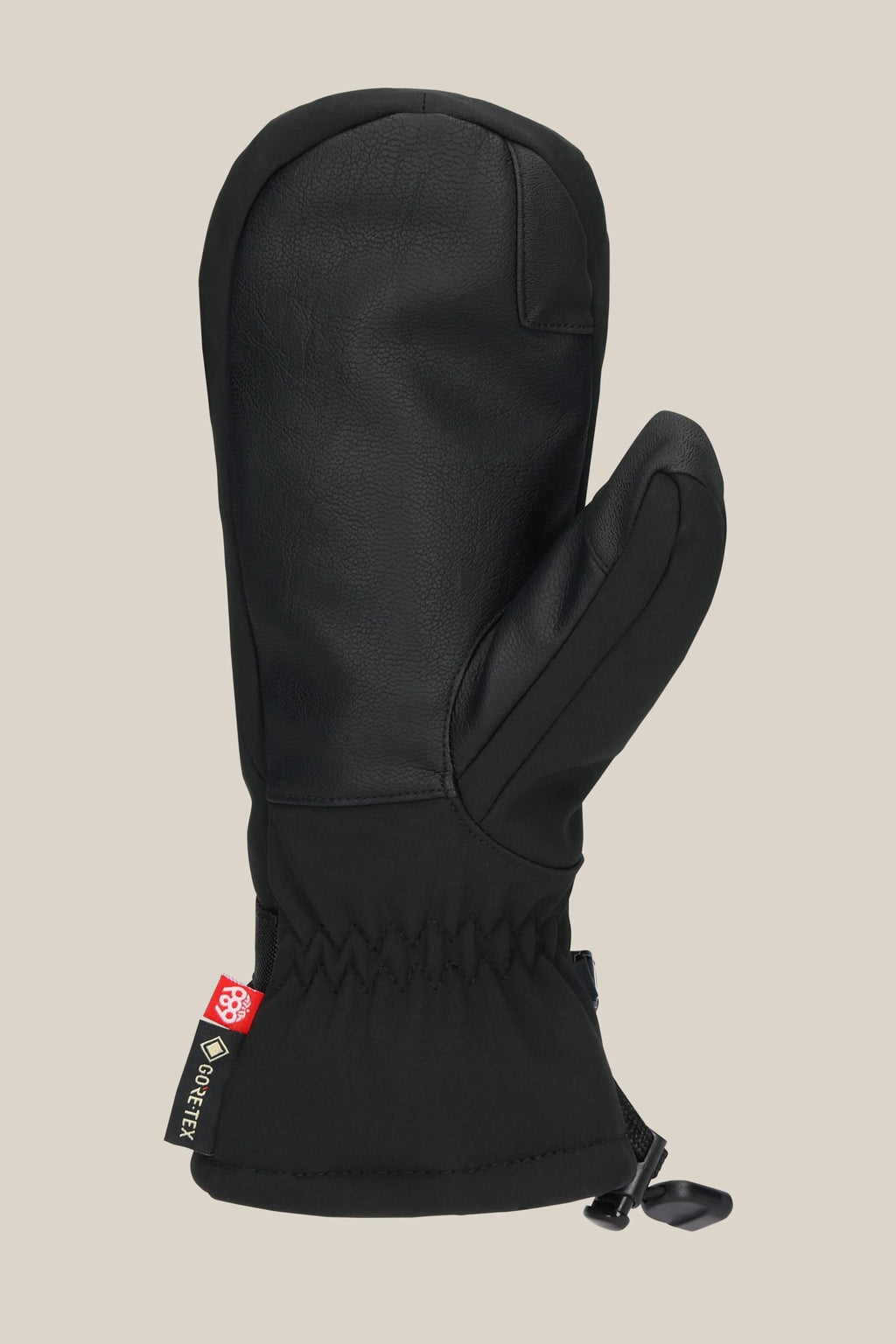 The 686 Women's GORE-TEX Linear™ Mitt in black, made from leather, poly, and PU fabric, has a cinched wrist, cuff drawstring, and GORE-TEX tag on the side. It's shown solo against a plain beige background.