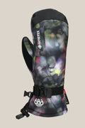 The 686 Women's GORE-TEX Linear™ Mitt features waterproof GORE-TEX, durable poly PU, an abstract black/green/purple design, adjustable wrist strap, and a 686 logo on the cuff. The mitt stands upright against a beige background.