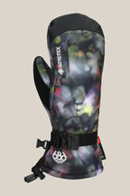 The 686 Women's GORE-TEX Linear™ Mitt features waterproof GORE-TEX, durable poly PU, an abstract black/green/purple design, adjustable wrist strap, and a 686 logo on the cuff. The mitt stands upright against a beige background.