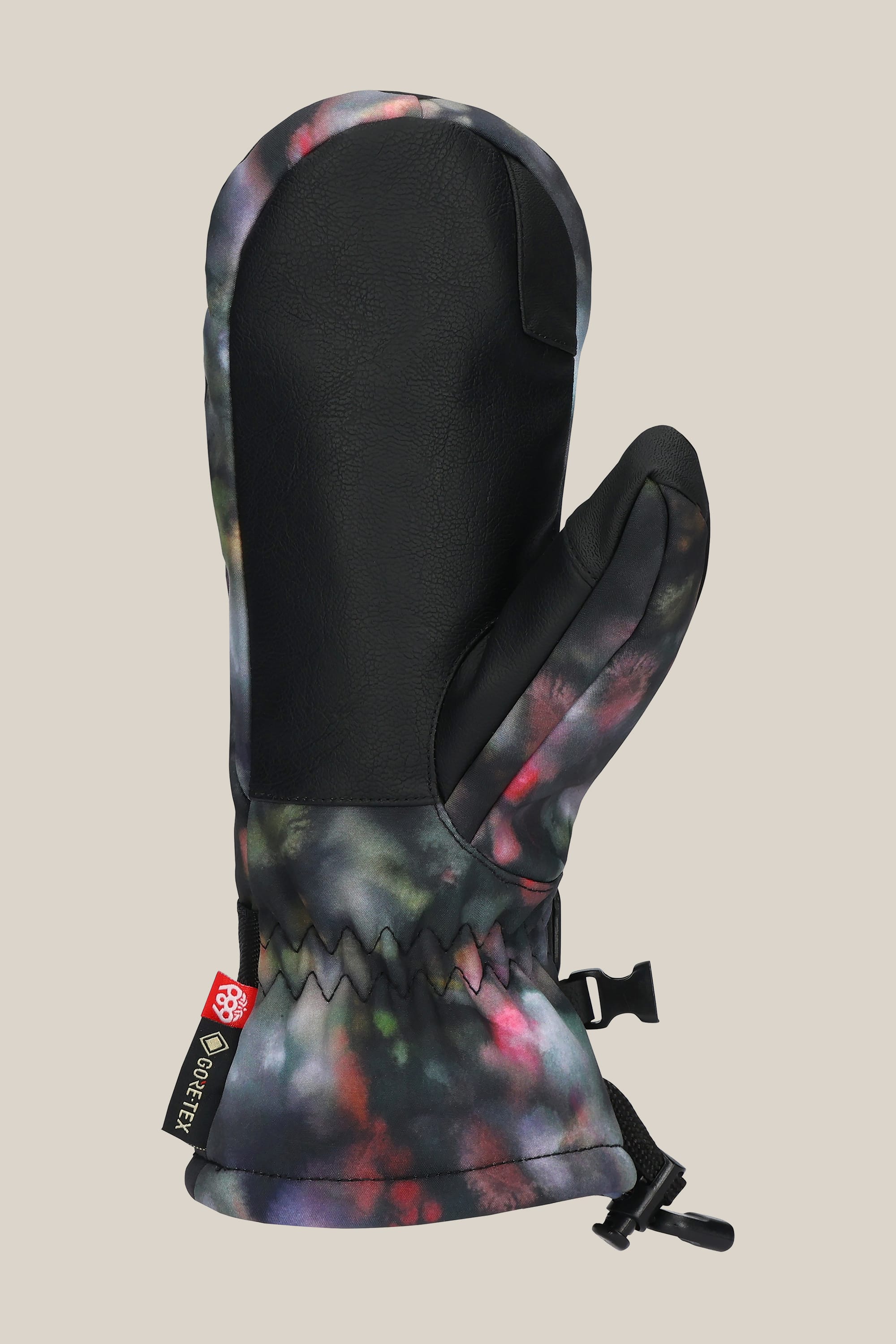 The 686 Women's GORE-TEX Linear™ Mitt features a black PU leather palm, vibrant tie-dye poly back, wrist strap, and small black buckle for a secure fit.