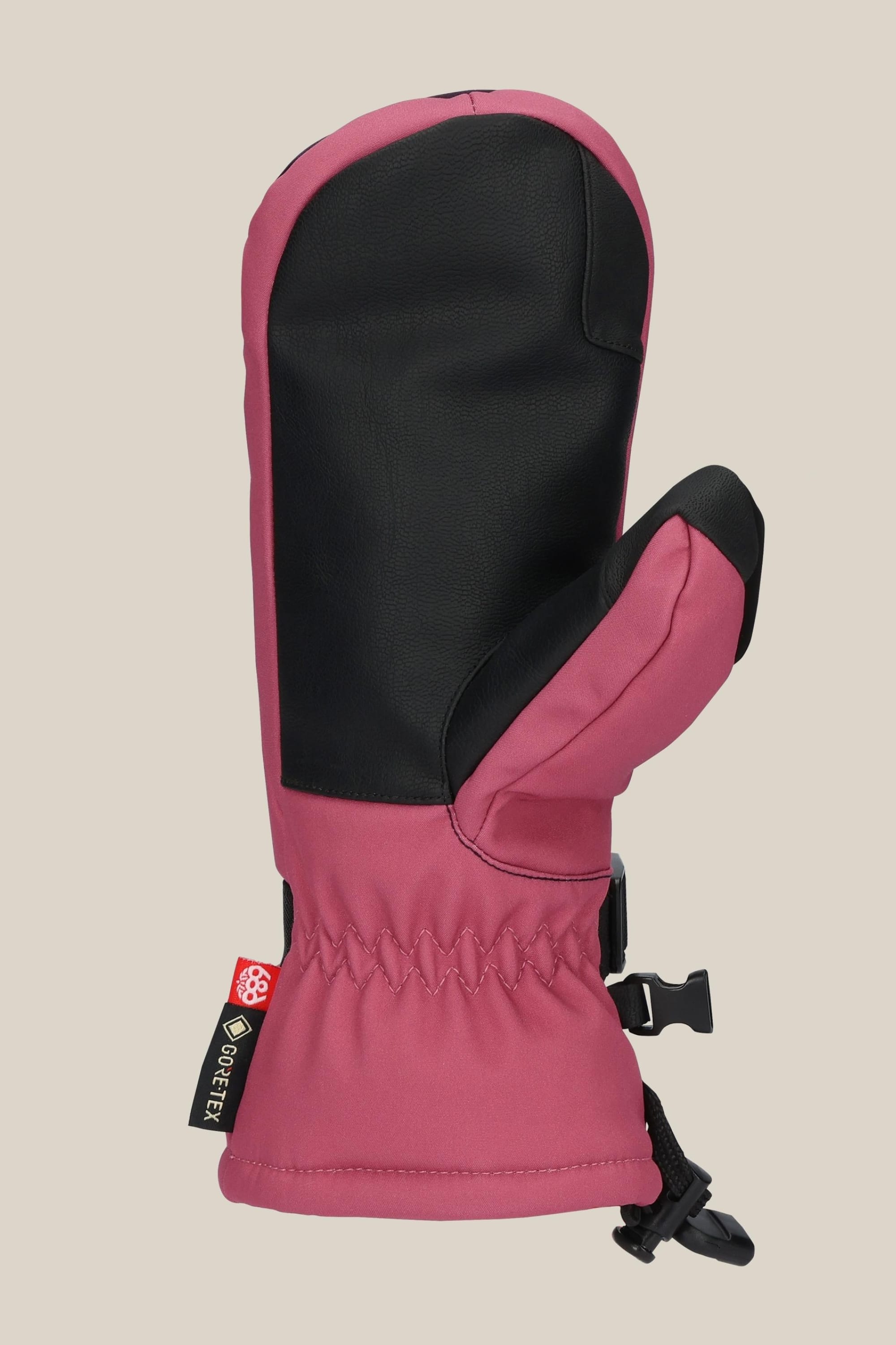 The 686 Women's GORE-TEX Linear™ Mitt, in pink and black with a black PU palm and thumb, features a gathered wrist, adjustable strap, poly lining, Gore-Tex tag, and brand tag, shown on a beige background.