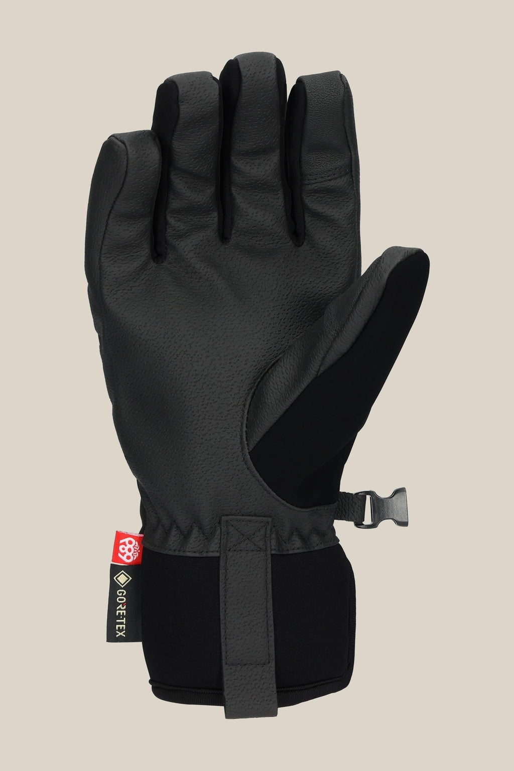 The 686 Women's GORE-TEX Linear™ Under Cuff Glove in black features a textured PU palm, adjustable wrist strap, and a small GORE-TEX tag, shown upright against a plain beige background.