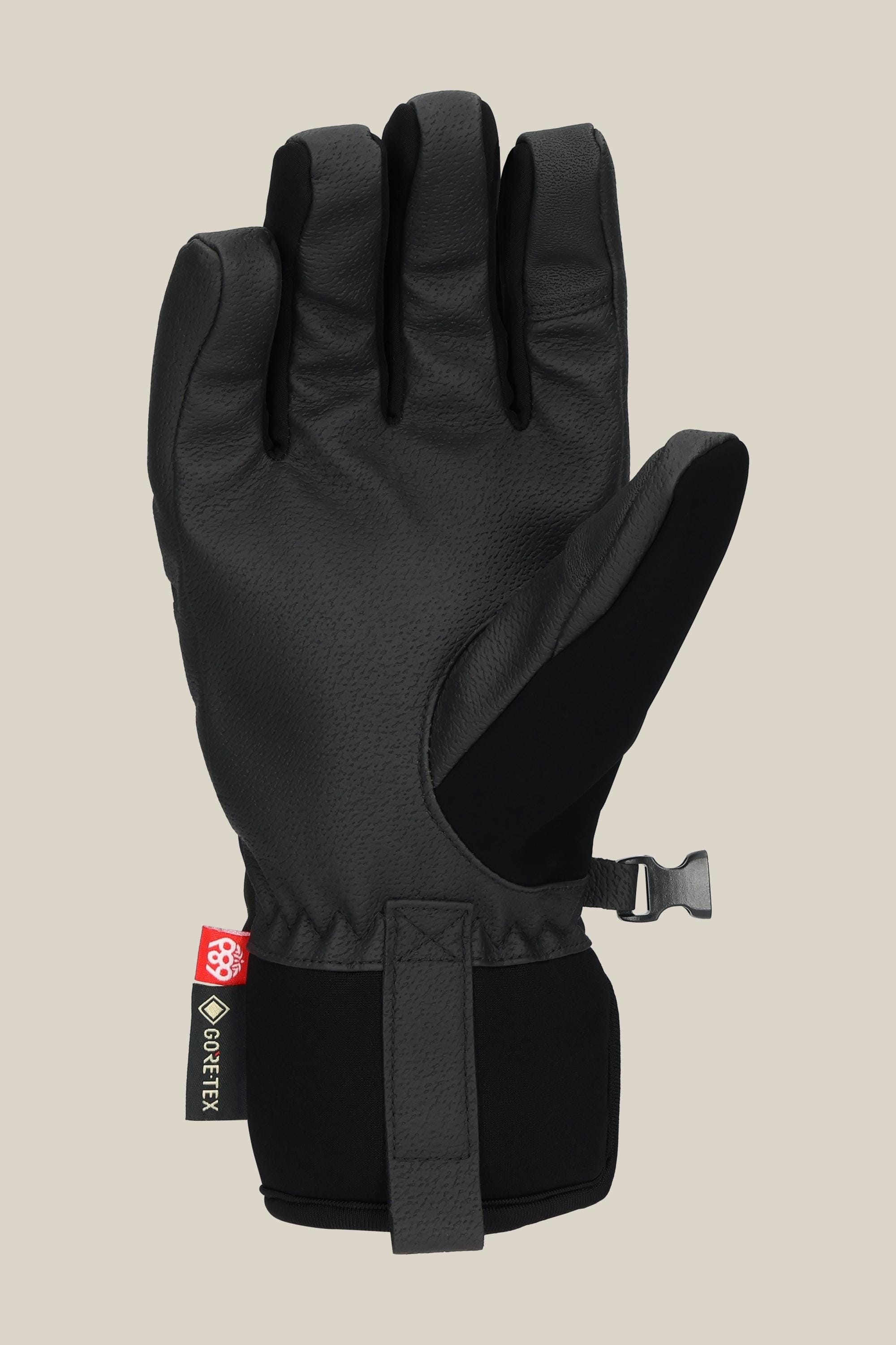 The 686 Women's GORE-TEX Linear™ Under Cuff Glove in black features a textured PU palm, adjustable wrist strap, and a small GORE-TEX tag, shown upright against a plain beige background.