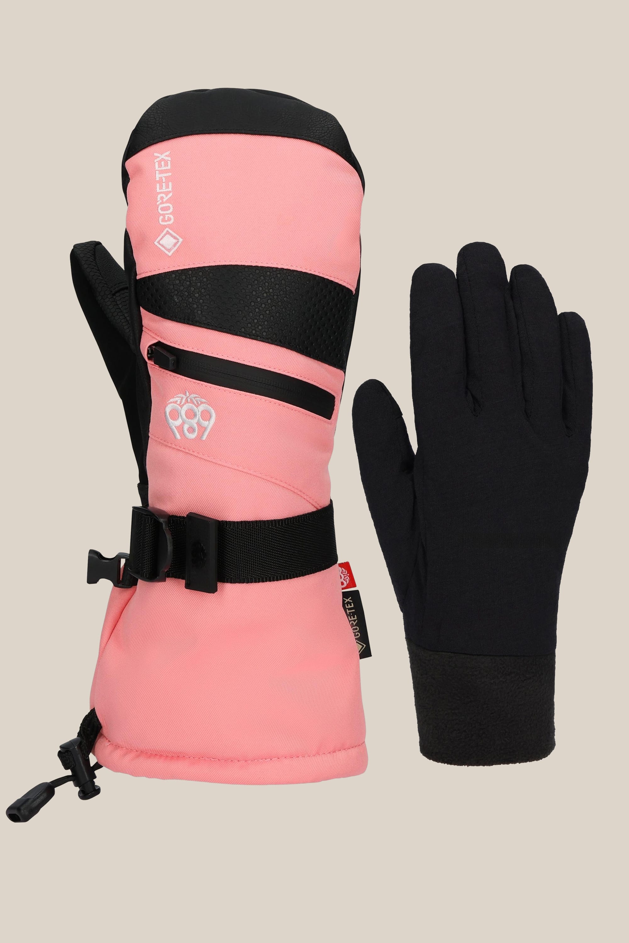 The 686 Women's GORE-TEX SMARTY® 3-In-1 Gauntlet Mitt in pink and black with an adjustable strap is displayed alongside a simple black glove, both resting on a plain beige background.
