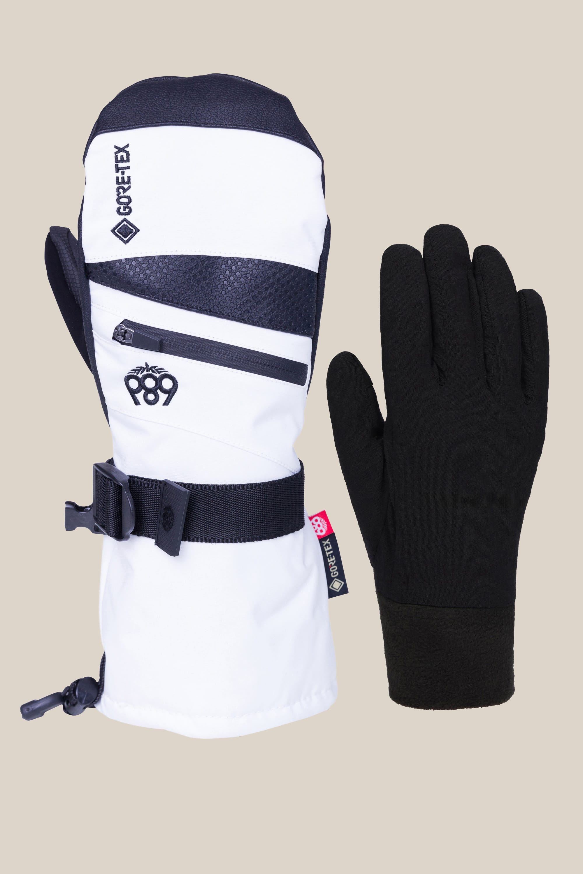 The image shows a 686 Women's GORE-TEX SMARTY® 3-In-1 Gauntlet Mitt in white, black, and grey with a Gore-Tex label, zipper, and wrist strap next to a plain black glove, both set against a simple background. Brand: 686.