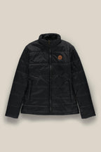 The 686 Womens Thermal Puff Insulated Jacket by 686 is a black quilted polyester jacket featuring a front zipper, two side pockets, and a brown circular patch on the left chest, shown against a beige background.