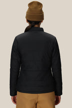 A person is shown from the back against a plain beige background, wearing a brown beanie, tan pants, and the 686 Womens Thermal Puff Insulated Jacket by 686.