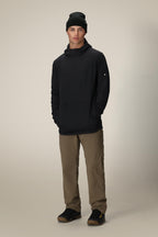 A person stands facing forward, hands casually in their pockets, wearing the 686 Men's Mission Grid™ Fleece Hoody in black with khaki pants and black shoes against a plain light background.