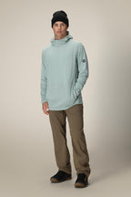 A young man wearing a black beanie, 686 Men's Mission Grid™ Fleece Hoody in light blue, khaki pants, and black sneakers stands facing the camera with his left hand in his pocket against a plain beige background.