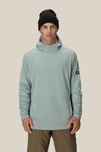 A man wears the 686 Men's Mission Grid™ Fleece Hoody in light gray, paired with a black beanie and brown pants, standing against a plain beige background.