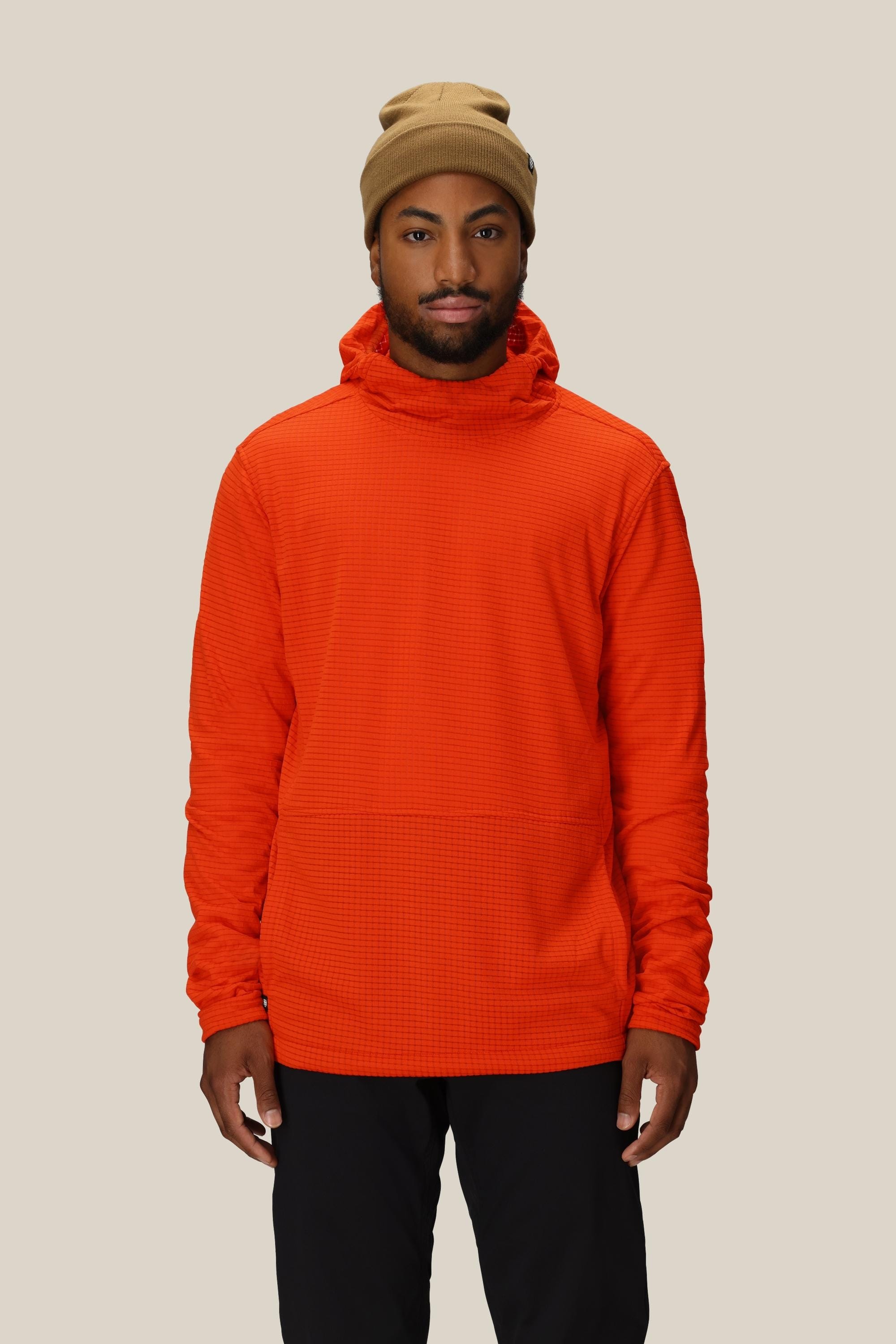 A man wearing a tan beanie, black pants, and the 686 Men's Mission Grid™ Fleece Hoody by 686 stands facing forward against a plain light beige background.